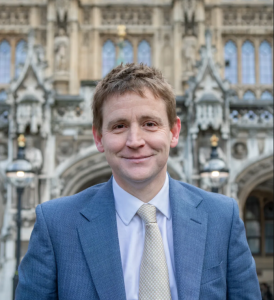UK electronics design and manufacturing, MP Mike Martin visits RVL. Image shows a professional headshot of Mike Martin's head and shoulders. He is standing in front of a building, which is blurred out behind him. He is wearing a blue jacket and a pale blue shirt, with a neutral coloured tie.